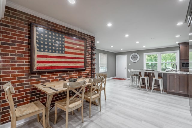 dining space with light hardwood / wood-style floors, crown molding, sink, and brick wall