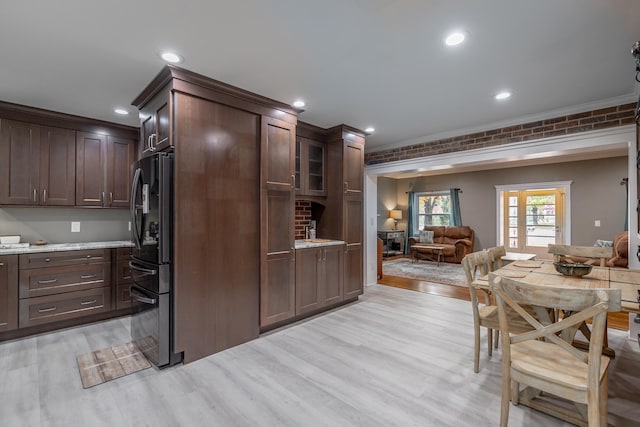 kitchen with light hardwood / wood-style flooring, dark brown cabinets, brick wall, stainless steel fridge, and light stone countertops