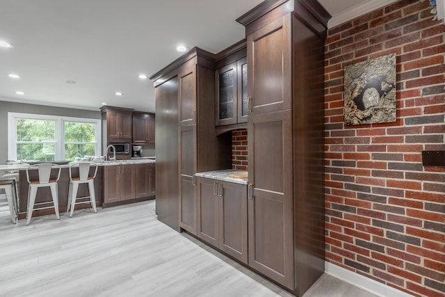 kitchen with light stone counters, crown molding, dark brown cabinets, and light wood-type flooring