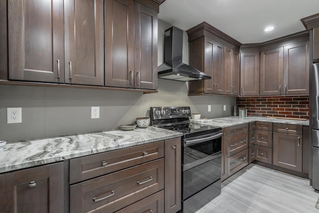 kitchen with wall chimney range hood, light stone countertops, light wood-type flooring, black electric range oven, and dark brown cabinetry