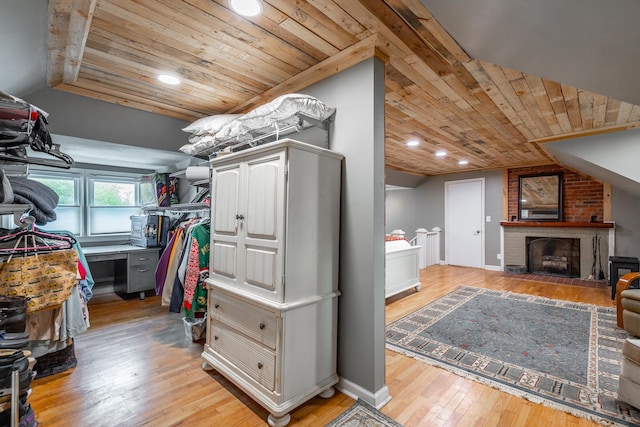 walk in closet with vaulted ceiling, a brick fireplace, and light hardwood / wood-style floors