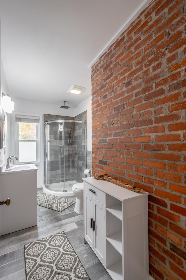 bathroom with hardwood / wood-style flooring, toilet, a shower with shower door, vanity, and brick wall