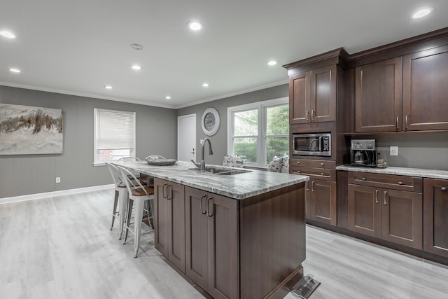 kitchen featuring stainless steel microwave, light hardwood / wood-style flooring, a center island with sink, ornamental molding, and sink