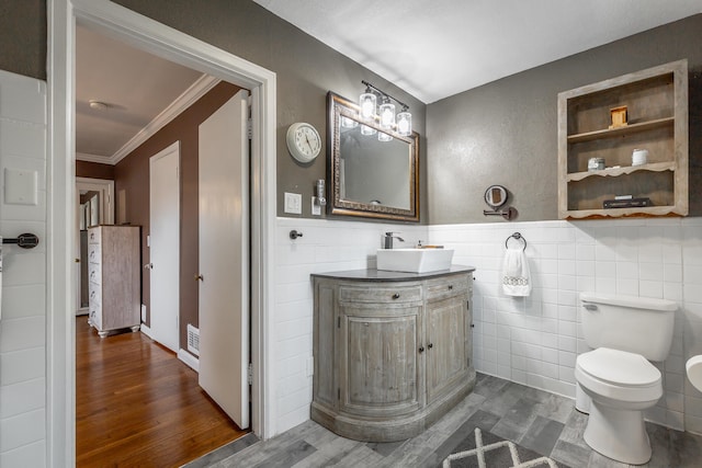 bathroom with toilet, wood-type flooring, vanity, ornamental molding, and tile walls