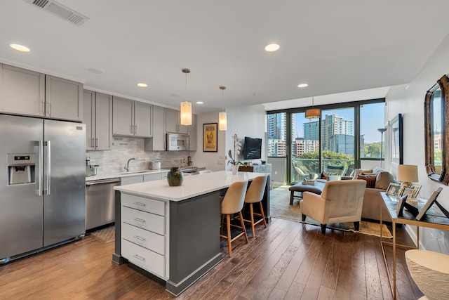 kitchen featuring a center island, stainless steel appliances, pendant lighting, gray cabinets, and dark wood-type flooring