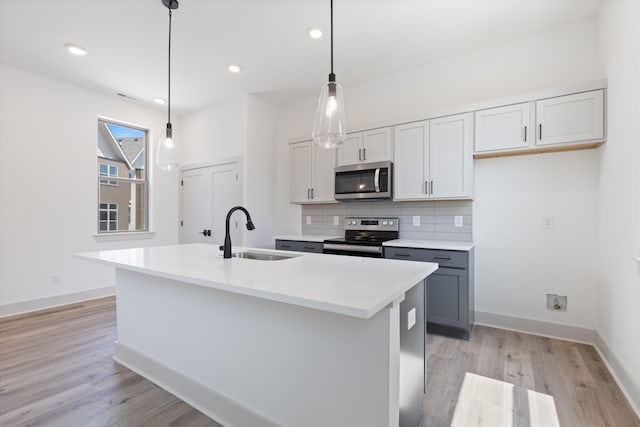 kitchen with an island with sink, light wood-type flooring, stainless steel appliances, sink, and decorative light fixtures