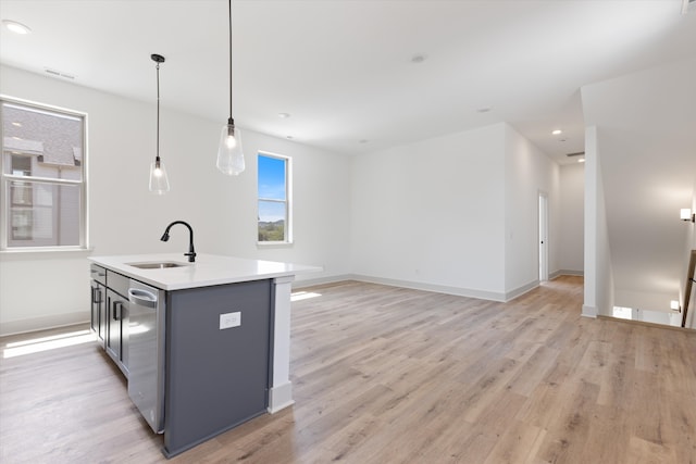 kitchen with a kitchen island with sink, stainless steel dishwasher, light hardwood / wood-style flooring, pendant lighting, and sink