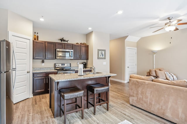 kitchen featuring dark brown cabinetry, a kitchen breakfast bar, a center island with sink, appliances with stainless steel finishes, and light wood-type flooring