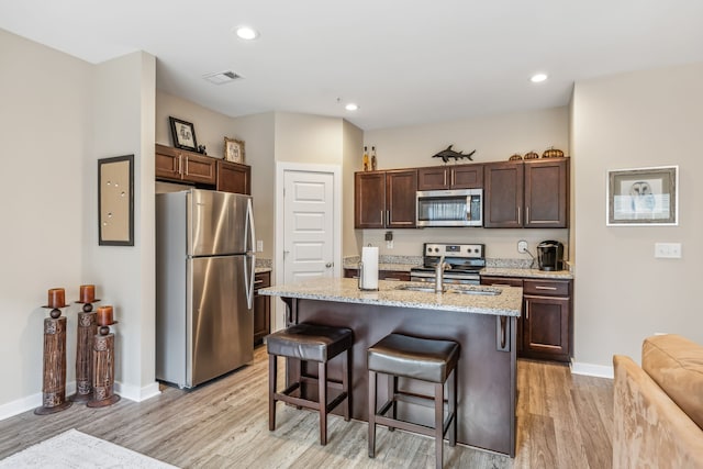 kitchen featuring light stone countertops, stainless steel appliances, an island with sink, a breakfast bar area, and light wood-type flooring