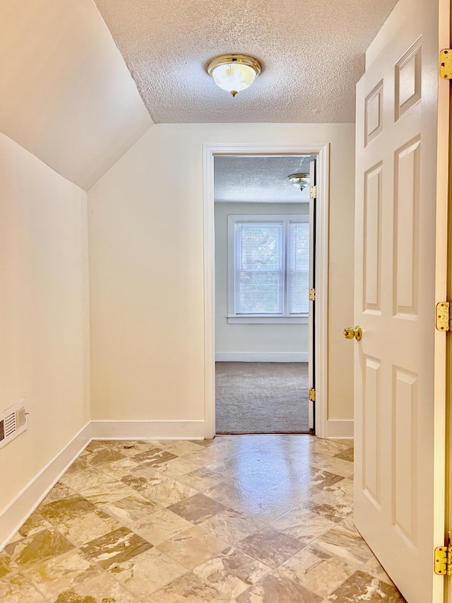 interior space with a textured ceiling, vaulted ceiling, and light colored carpet