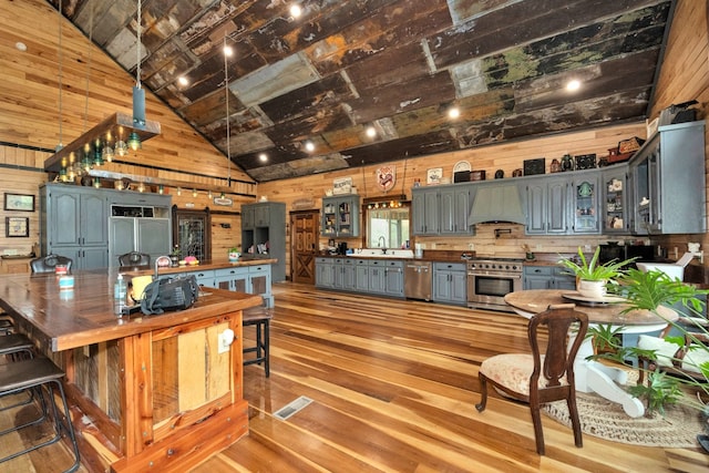 kitchen featuring light hardwood / wood-style floors, vaulted ceiling, wooden walls, high end appliances, and premium range hood