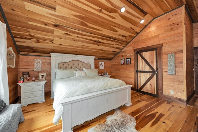 bedroom with lofted ceiling, wood ceiling, a barn door, light hardwood / wood-style flooring, and wooden walls