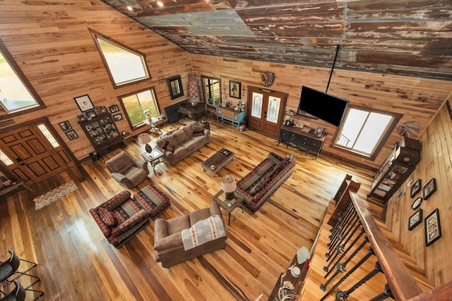 unfurnished living room with high vaulted ceiling, wood walls, wood-type flooring, and a wealth of natural light