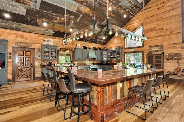 bar with extractor fan, wooden walls, high end range, light wood-type flooring, and high vaulted ceiling