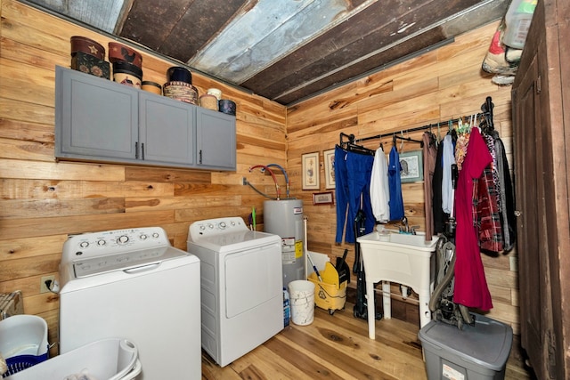 laundry room featuring washer and clothes dryer, water heater, light hardwood / wood-style flooring, cabinets, and wood walls