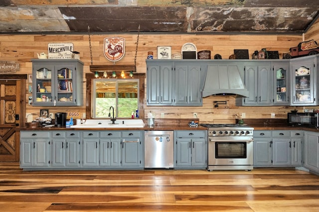 kitchen featuring sink, custom exhaust hood, stainless steel appliances, and wood walls