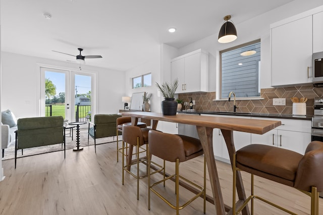 kitchen with white cabinetry, backsplash, hanging light fixtures, light hardwood / wood-style flooring, and wood counters