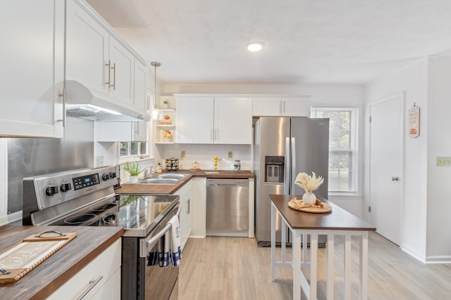 kitchen featuring appliances with stainless steel finishes, pendant lighting, a healthy amount of sunlight, and butcher block counters