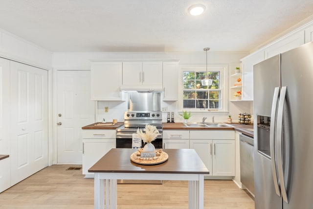 kitchen featuring white cabinetry, butcher block counters, stainless steel appliances, and pendant lighting