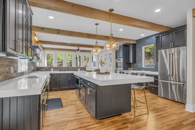 kitchen featuring a kitchen island, built in appliances, a breakfast bar, decorative light fixtures, and light wood-type flooring