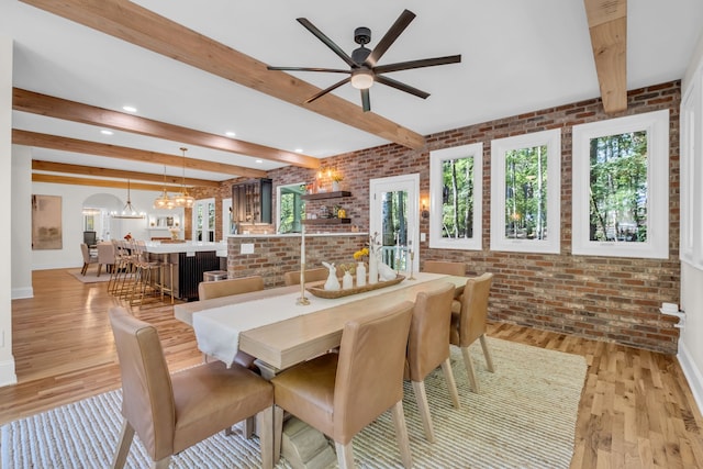 dining space featuring beam ceiling, brick wall, light hardwood / wood-style flooring, and ceiling fan with notable chandelier