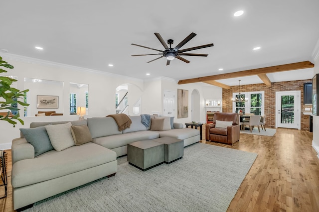 living room featuring beam ceiling, ornamental molding, ceiling fan with notable chandelier, light hardwood / wood-style floors, and brick wall