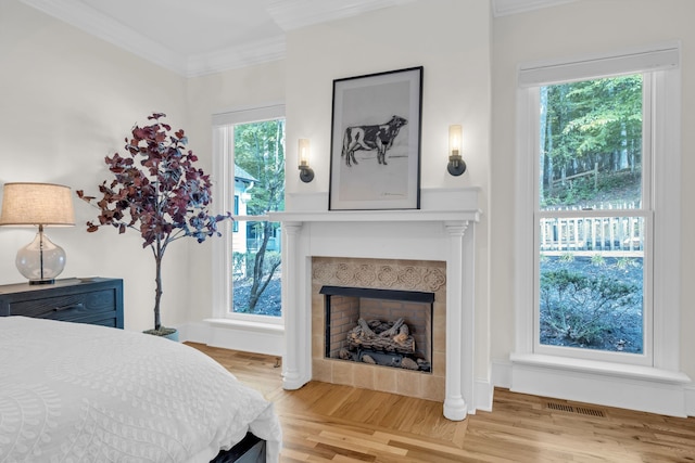 bedroom with ornamental molding, a tile fireplace, and light hardwood / wood-style floors