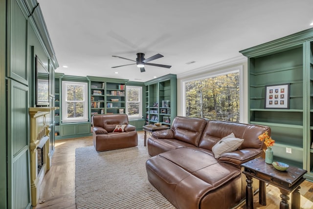 living room featuring crown molding, built in shelves, light wood-type flooring, and ceiling fan