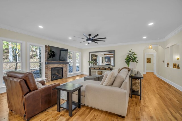 living room with crown molding, light hardwood / wood-style flooring, a brick fireplace, and ceiling fan