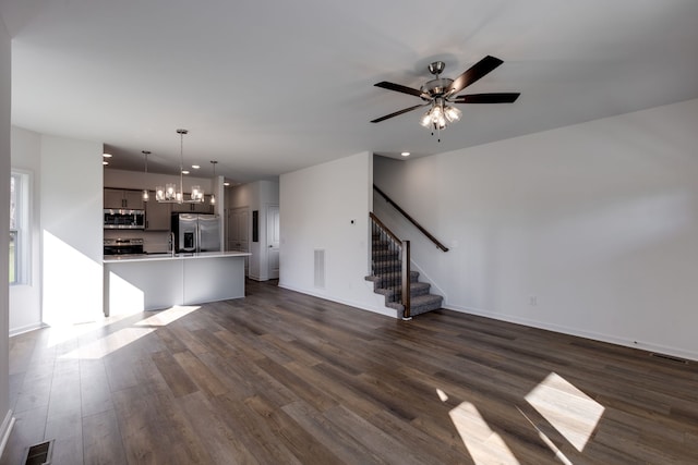 unfurnished living room featuring ceiling fan with notable chandelier and dark hardwood / wood-style flooring