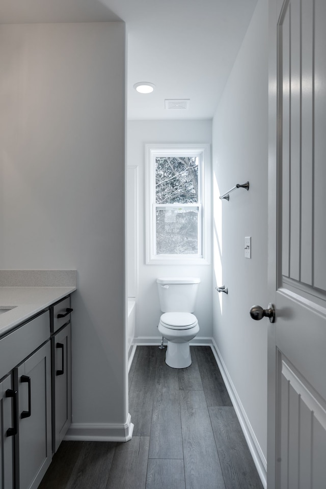 bathroom with a bath, vanity, wood-type flooring, and toilet