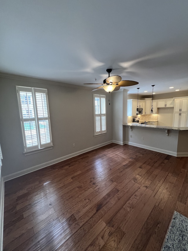 unfurnished living room featuring ornamental molding, ceiling fan, and dark hardwood / wood-style flooring