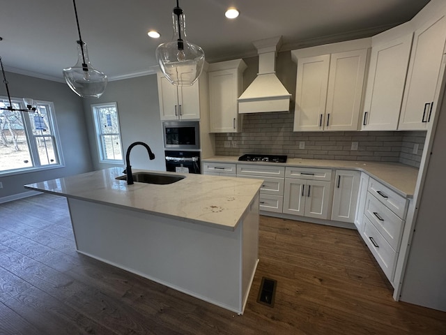 kitchen featuring sink, premium range hood, white cabinetry, black appliances, and a center island with sink