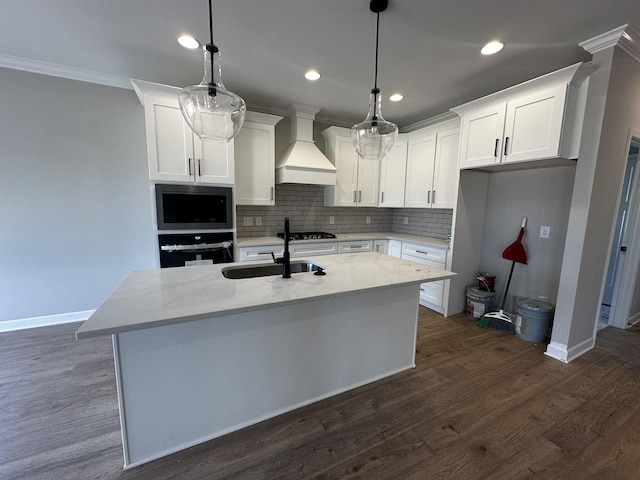 kitchen featuring pendant lighting, custom exhaust hood, oven, and an island with sink