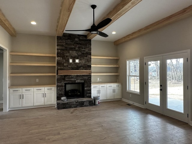 unfurnished living room featuring french doors, a stone fireplace, built in features, beamed ceiling, and light hardwood / wood-style floors