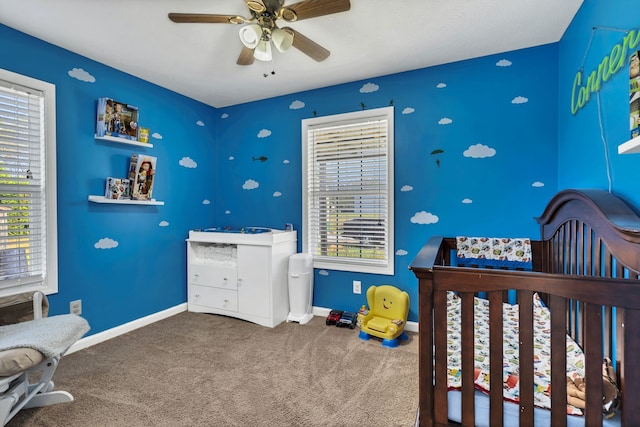 bedroom with carpet flooring, a nursery area, multiple windows, and ceiling fan