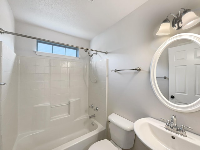 full bathroom with a textured ceiling, tiled shower / bath combo, toilet, and sink