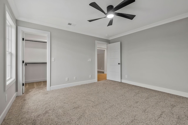 unfurnished bedroom with light carpet, a spacious closet, ceiling fan, and ornamental molding