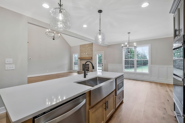 kitchen with a fireplace, sink, decorative light fixtures, dishwasher, and an island with sink