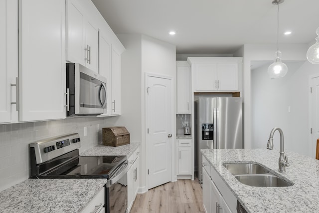 kitchen featuring sink, white cabinets, pendant lighting, appliances with stainless steel finishes, and light hardwood / wood-style floors