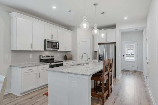 kitchen featuring a kitchen island with sink, sink, light stone countertops, white cabinetry, and appliances with stainless steel finishes