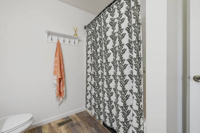 bathroom featuring a textured ceiling, curtained shower, hardwood / wood-style flooring, and toilet