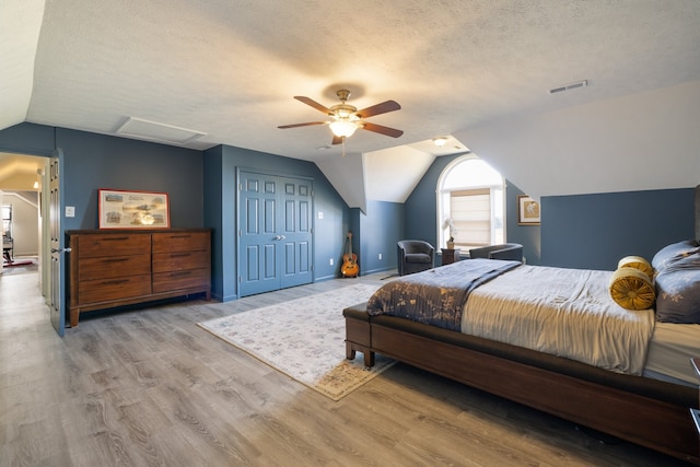 bedroom featuring a closet, light hardwood / wood-style flooring, vaulted ceiling, a textured ceiling, and ceiling fan