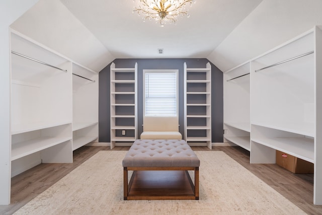 walk in closet featuring an inviting chandelier, wood-type flooring, and vaulted ceiling