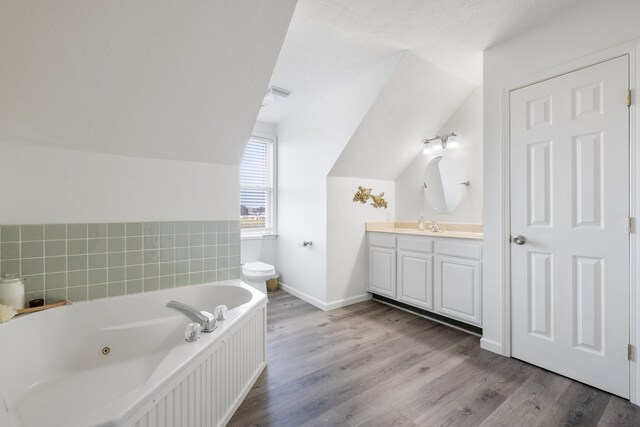 bathroom with lofted ceiling, hardwood / wood-style floors, a textured ceiling, vanity, and a tub to relax in