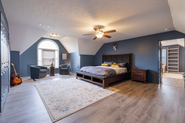 bedroom with a textured ceiling, vaulted ceiling, wood-type flooring, and ceiling fan