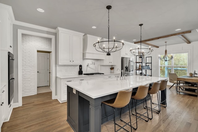 kitchen with stainless steel fridge, dark hardwood / wood-style floors, decorative light fixtures, white cabinets, and a center island with sink