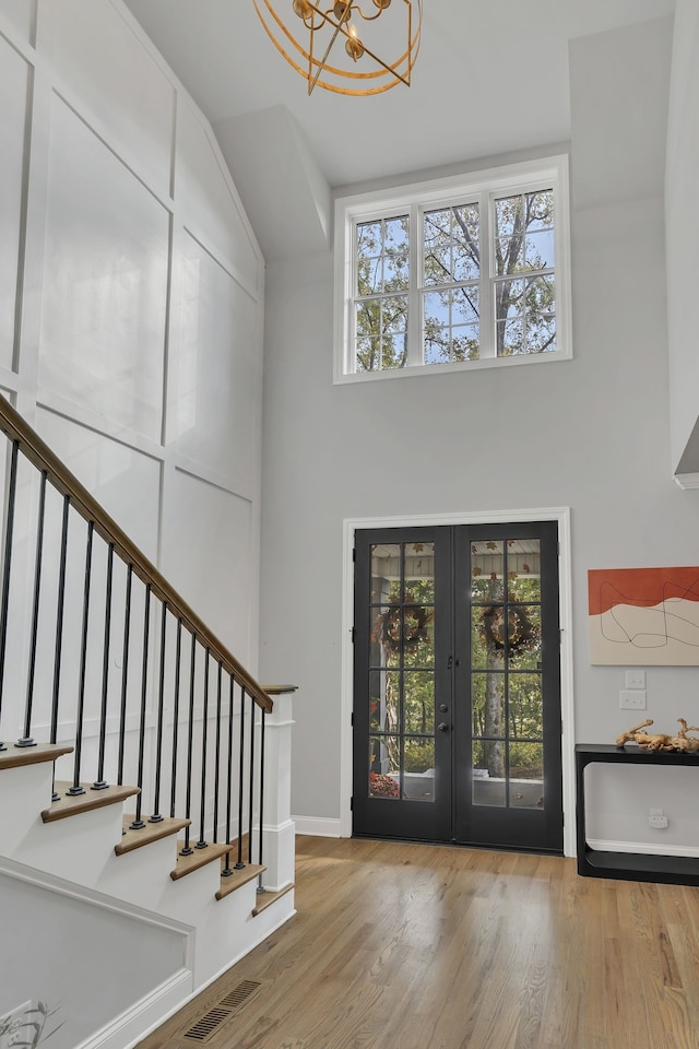 entrance foyer with french doors, light hardwood / wood-style flooring, a notable chandelier, and a healthy amount of sunlight