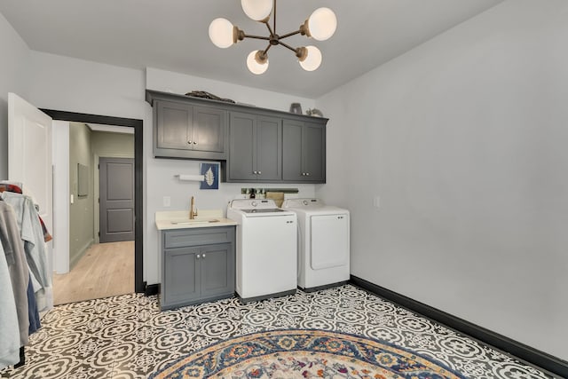 clothes washing area with sink, light wood-type flooring, washing machine and clothes dryer, cabinets, and a chandelier