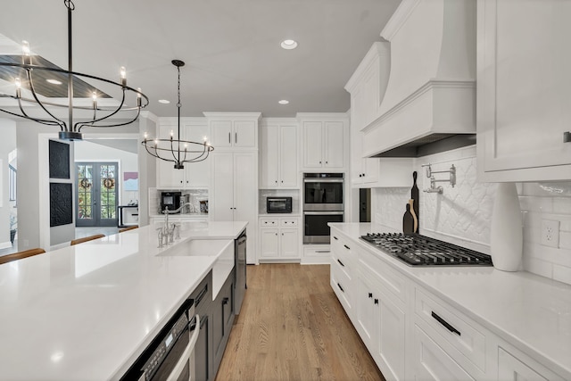 kitchen with appliances with stainless steel finishes, hanging light fixtures, white cabinetry, light hardwood / wood-style floors, and premium range hood